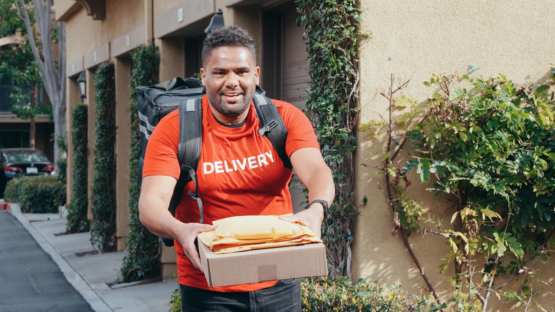 Kurier w czerwonym uniformie niesie paczki podczas słonecznego dnia