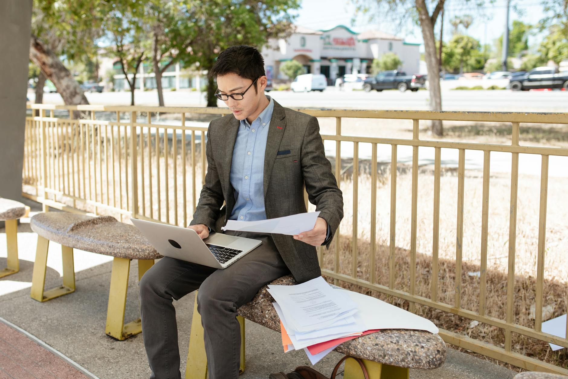 Młody mężczyzna analizuje dokumenty gwarancyjne przy laptopie w parku