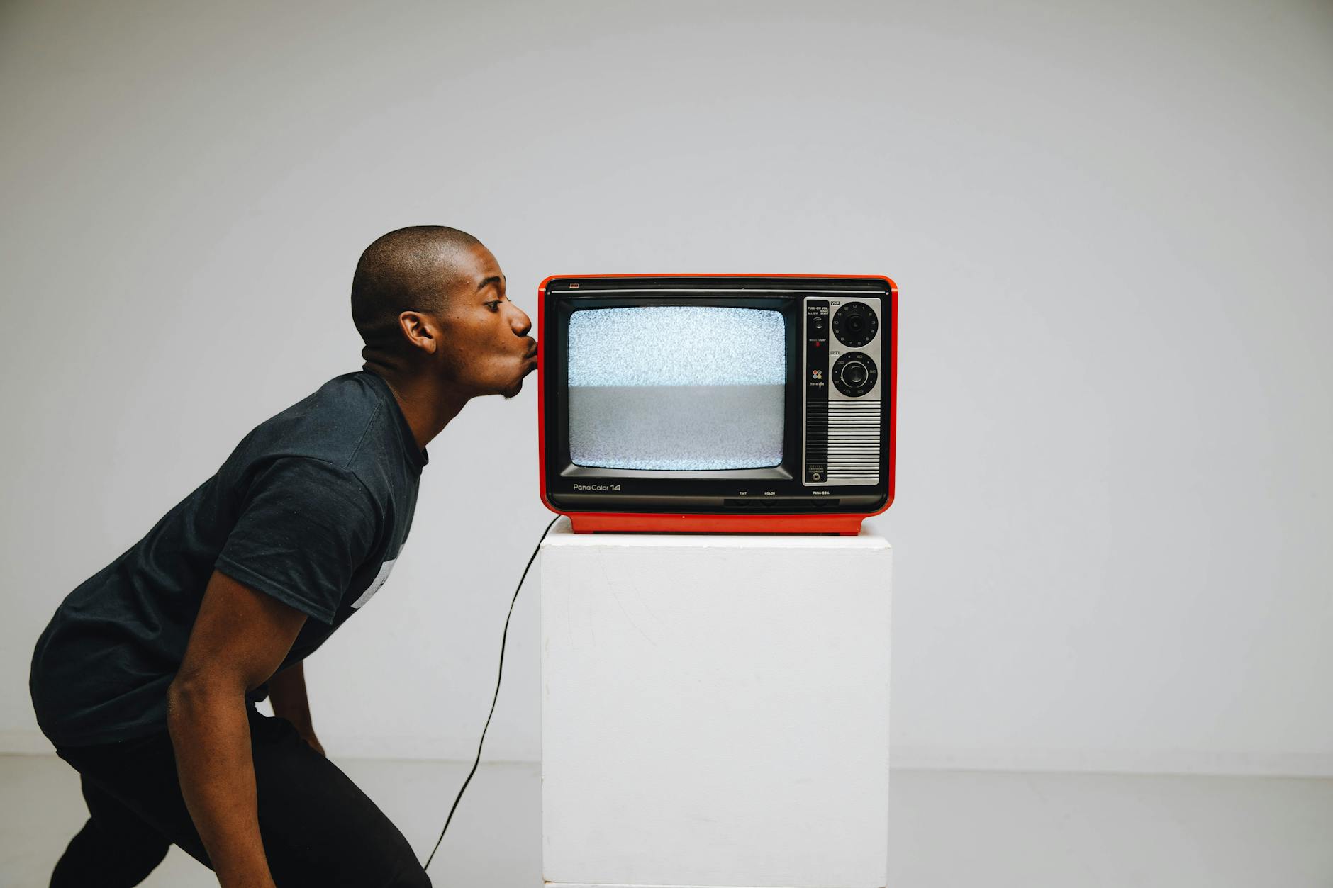 Mężczyzna całuje czerwony retro telewizor w minimalistycznym studio