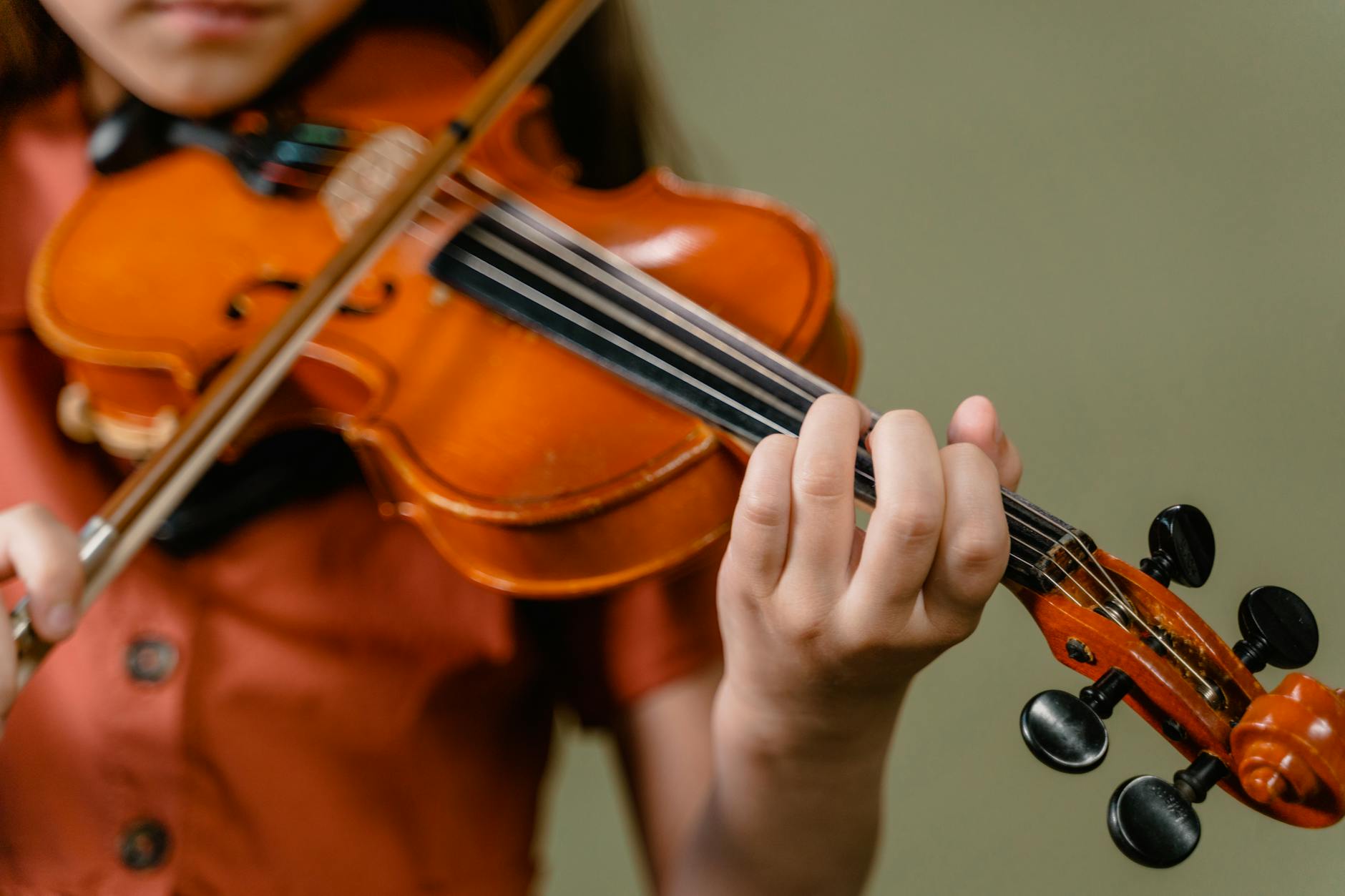 Pierwsze instrumenty dla dzieci: jak wybrać, kiedy zacząć i jak wspierać rozwój muzyczny smyka Dziecko grające na skrzypcach w domu, zbliżenie na dłoń i struny