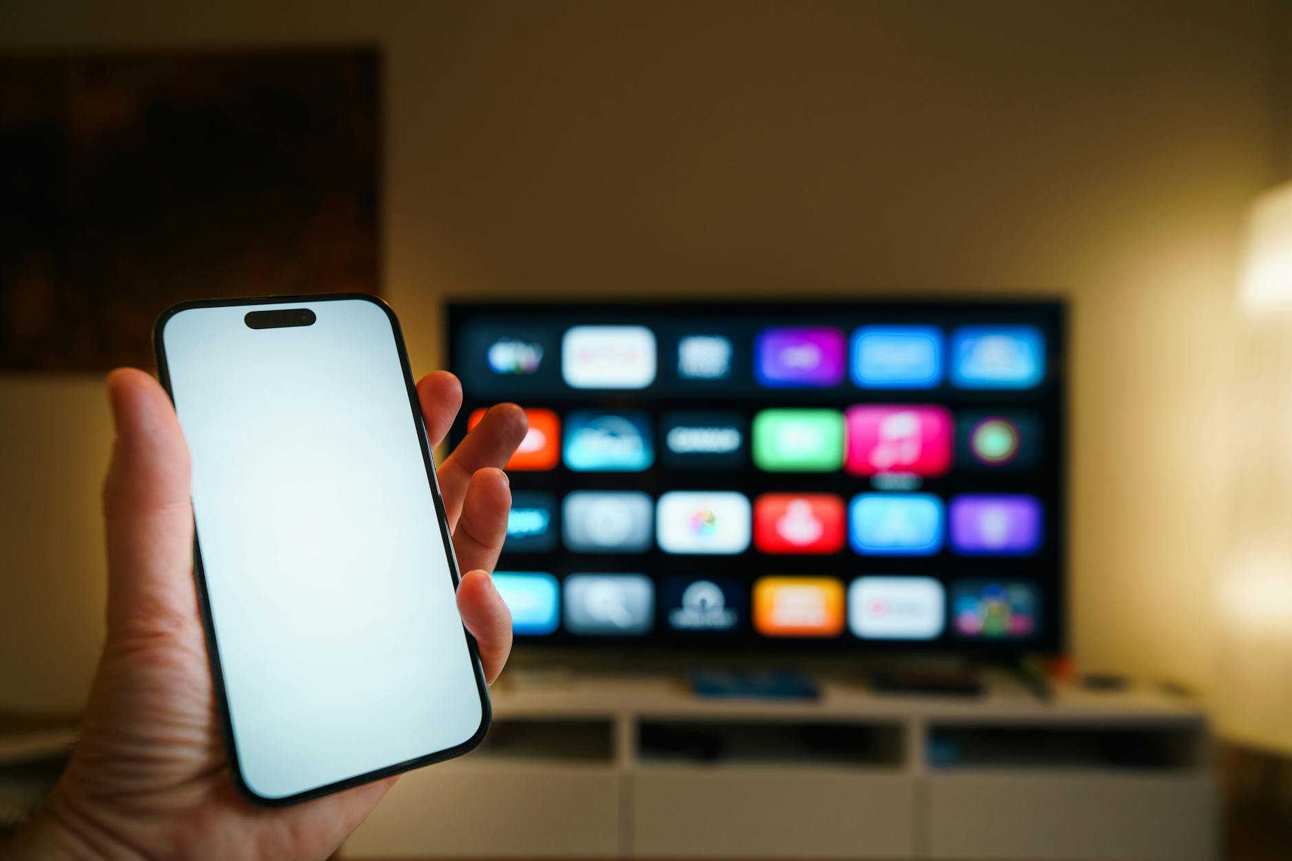 Smartfon przed telewizorem Smart TV z wyświetlonymi aplikacjami