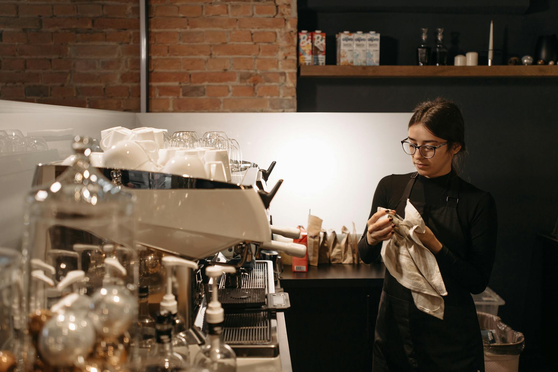 Barista czyści ekspres do kawy w stylowej kawiarni z ceglaną ścianą