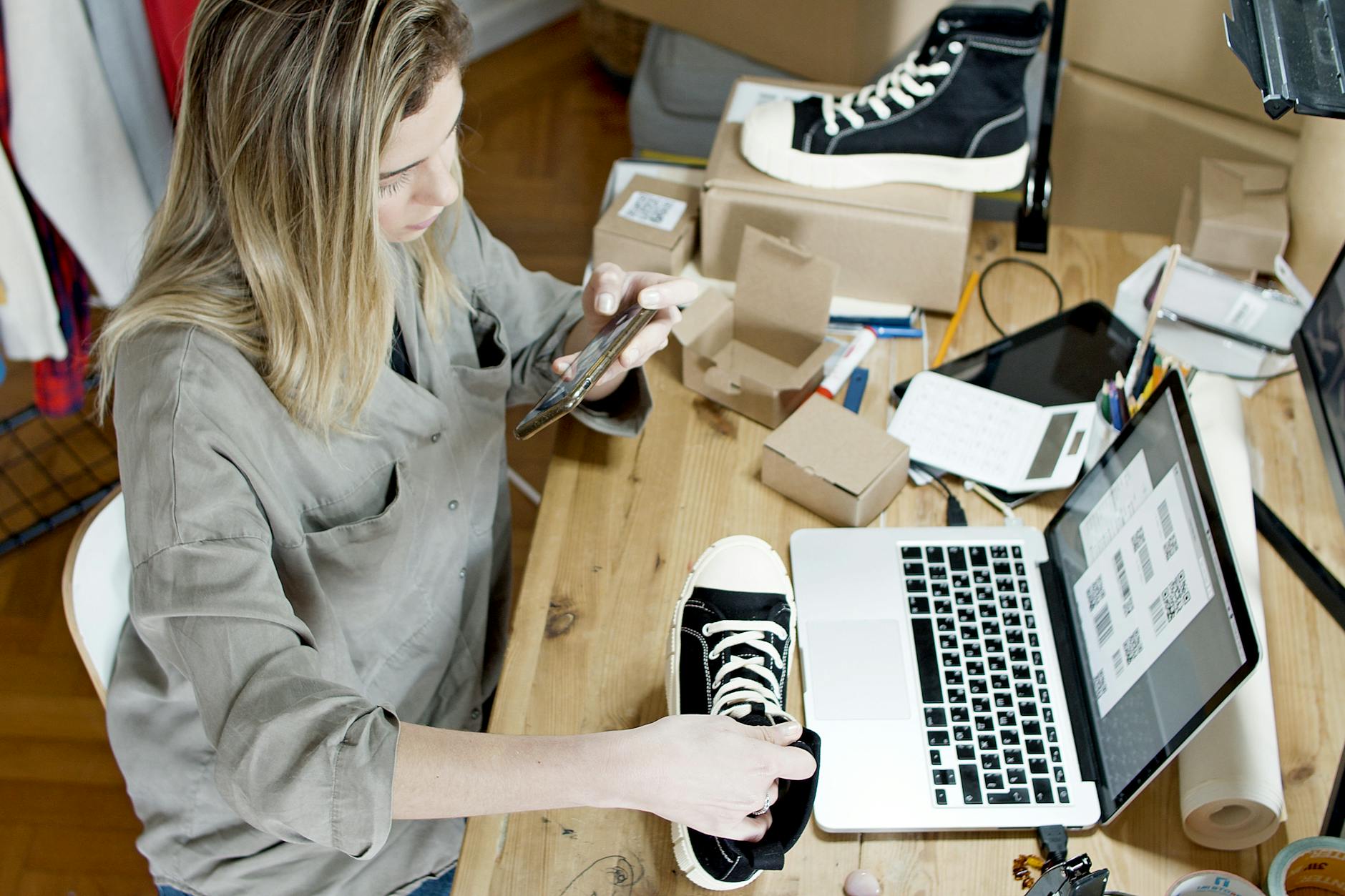 Kobieta fotografuje buty na sprzedaż online przy laptopie i paczkach