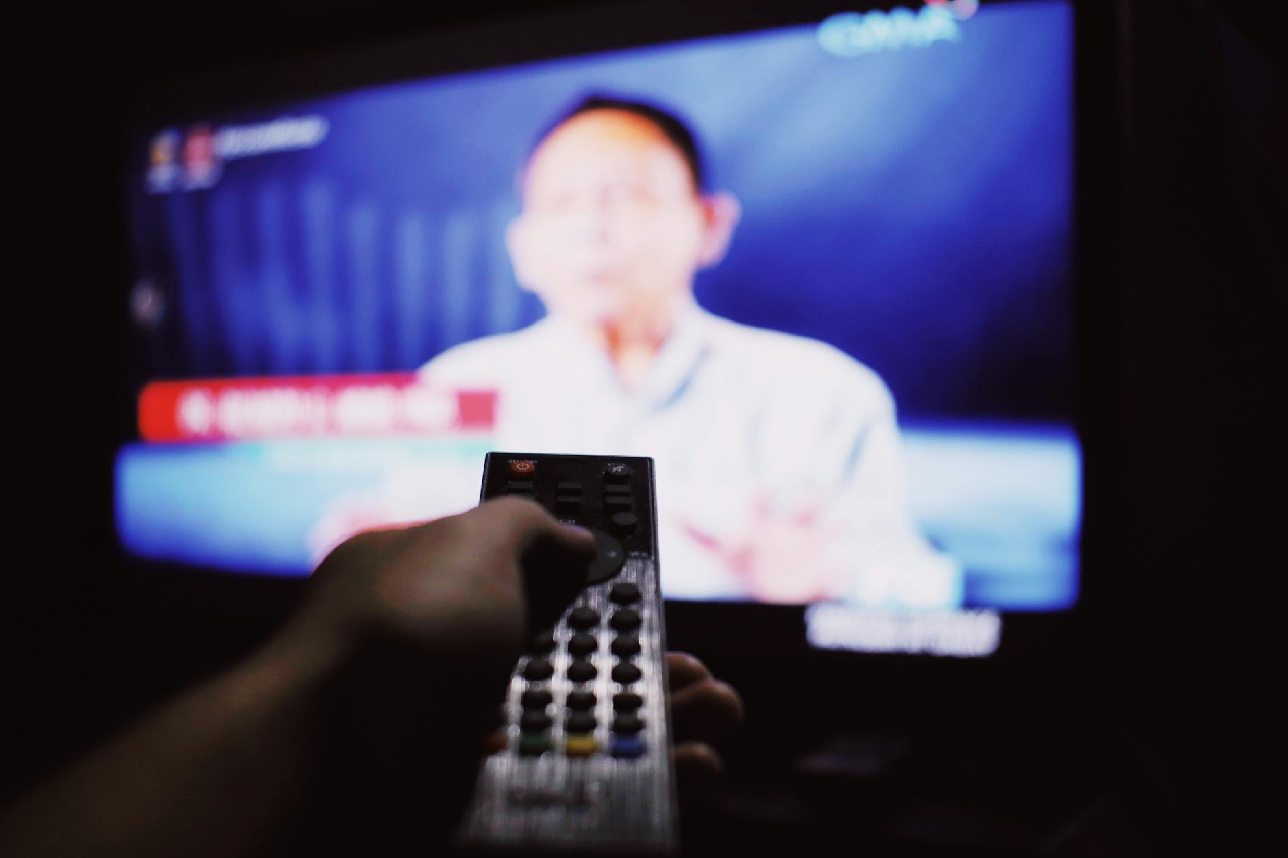 Osoba w zaciemnionym salonie przełącza kanały telewizora pilotem