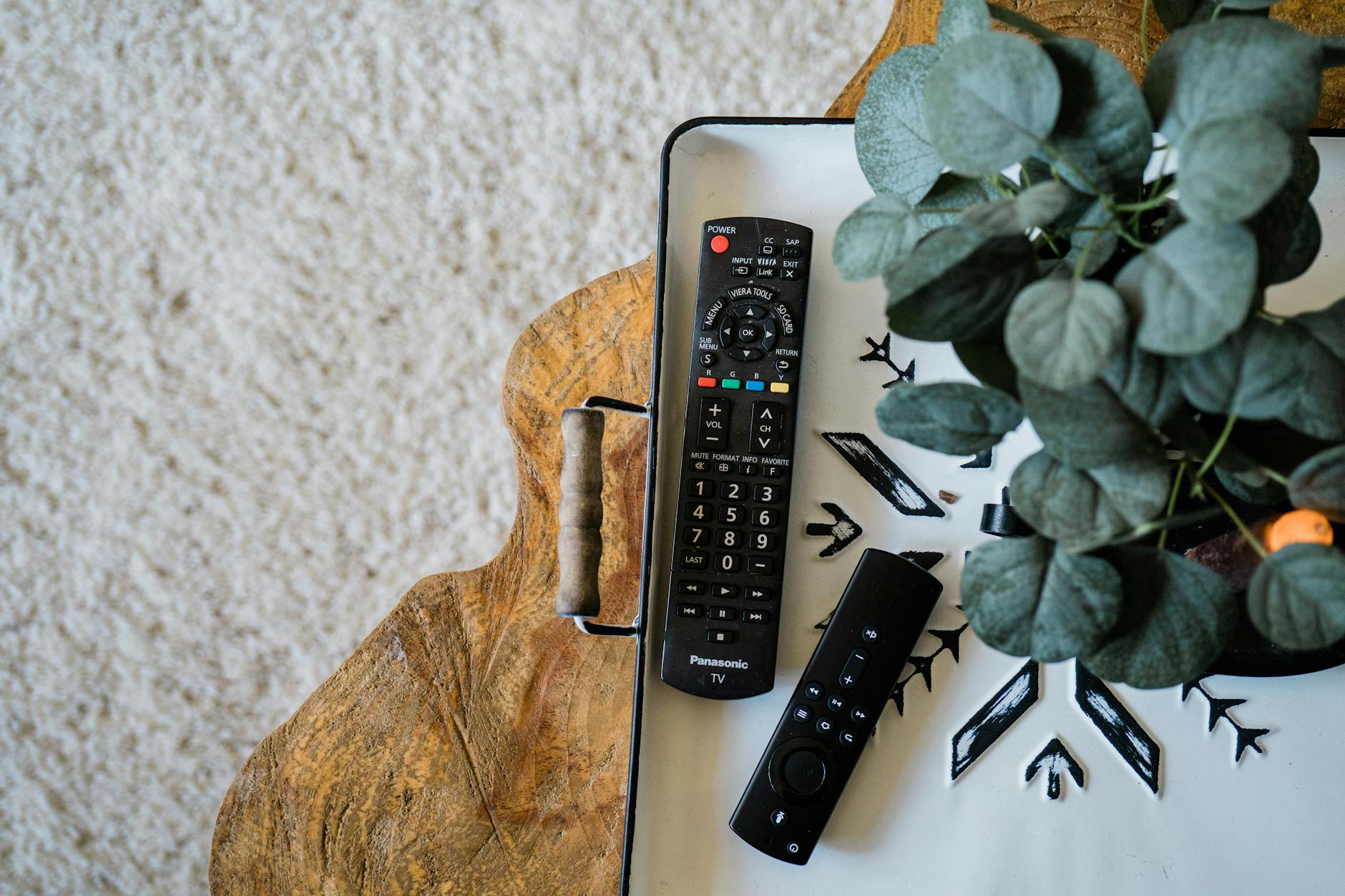 Kable, pilot, nóżki, uchwyt: checklista akcesoriów do TV z outletu Piloty do telewizora obok rośliny na drewnianym stoliku z góry