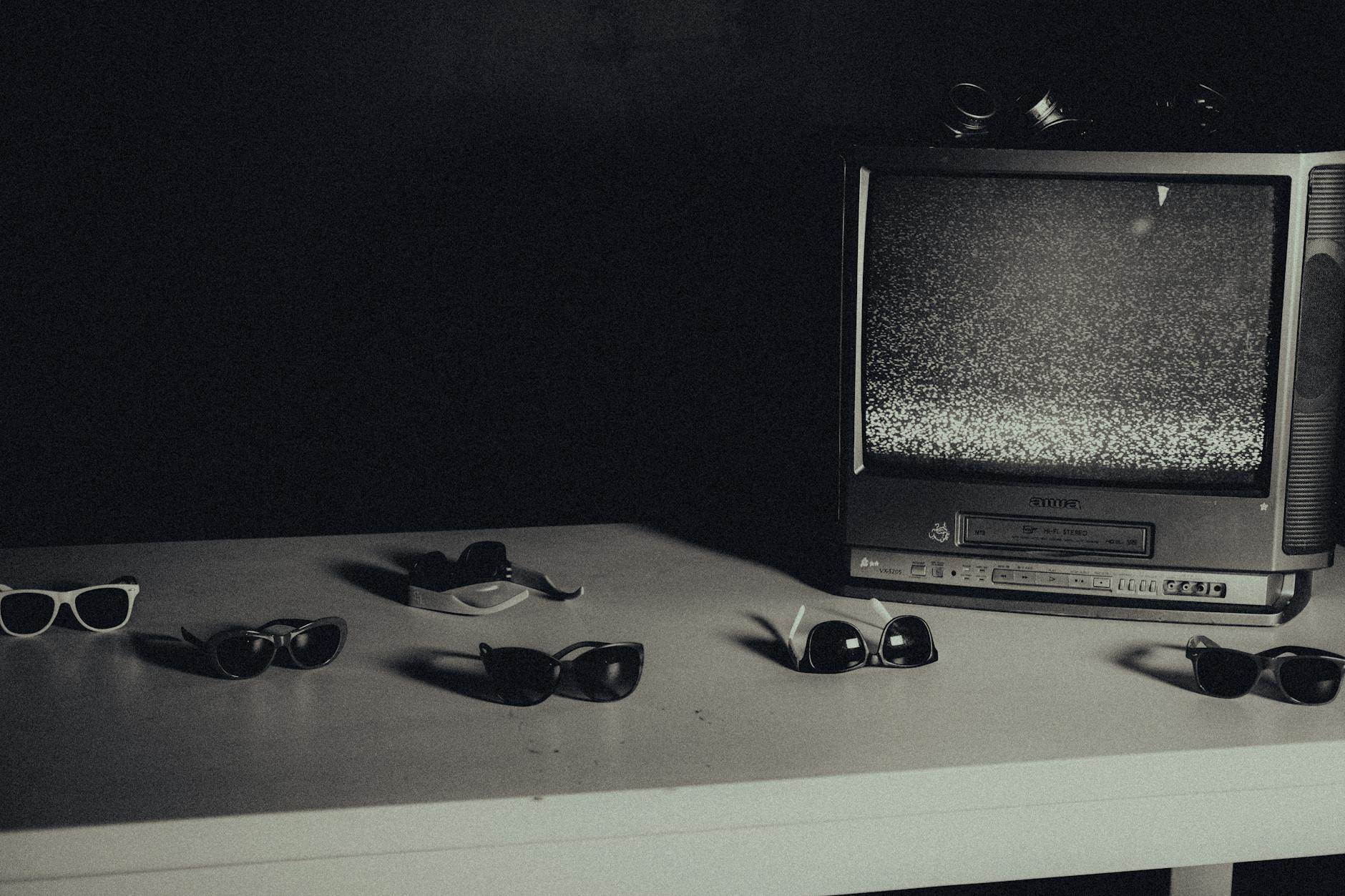 Stary telewizor z śniegiem na ekranie i kilka okularów na białym stole