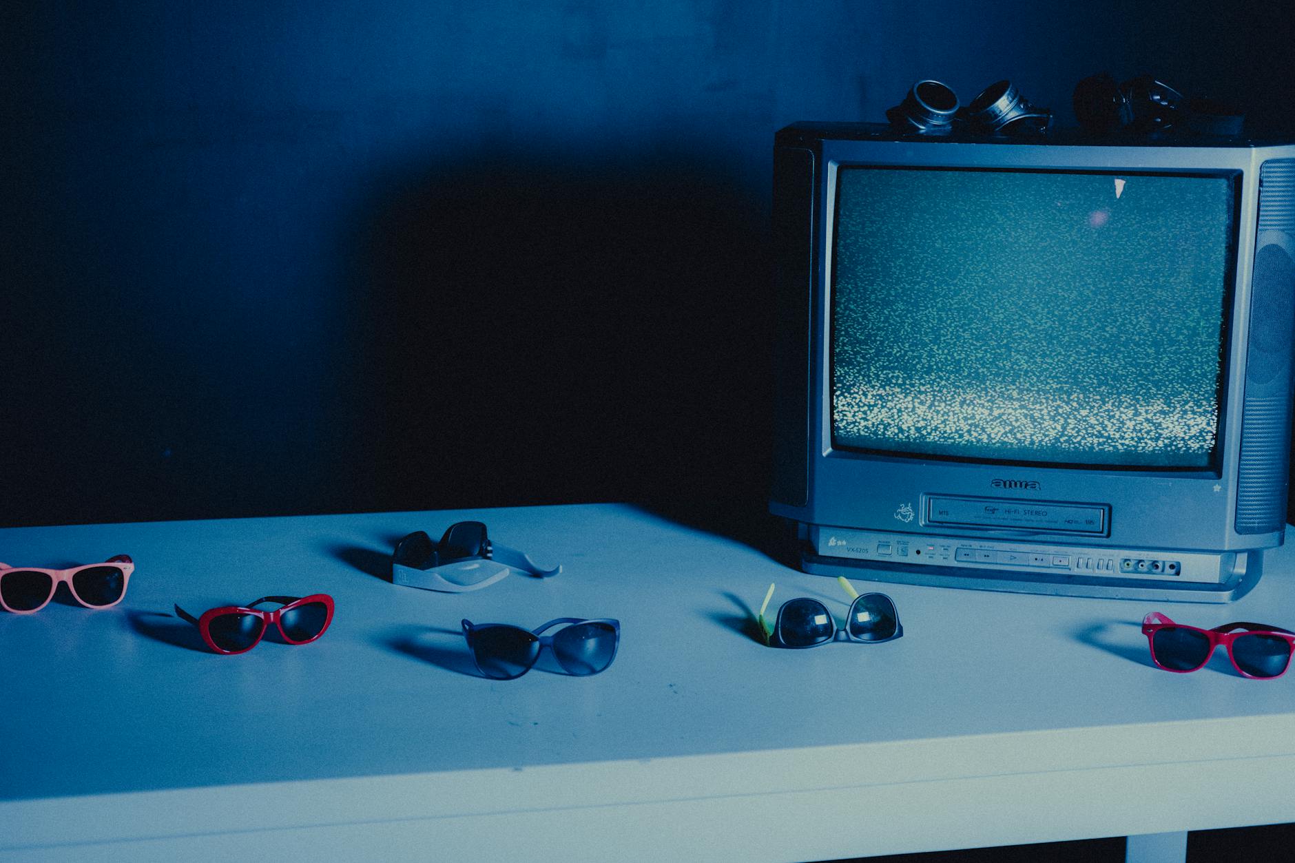 Stary telewizor z szumem otoczony kolorowymi okularami na niebieskim tle