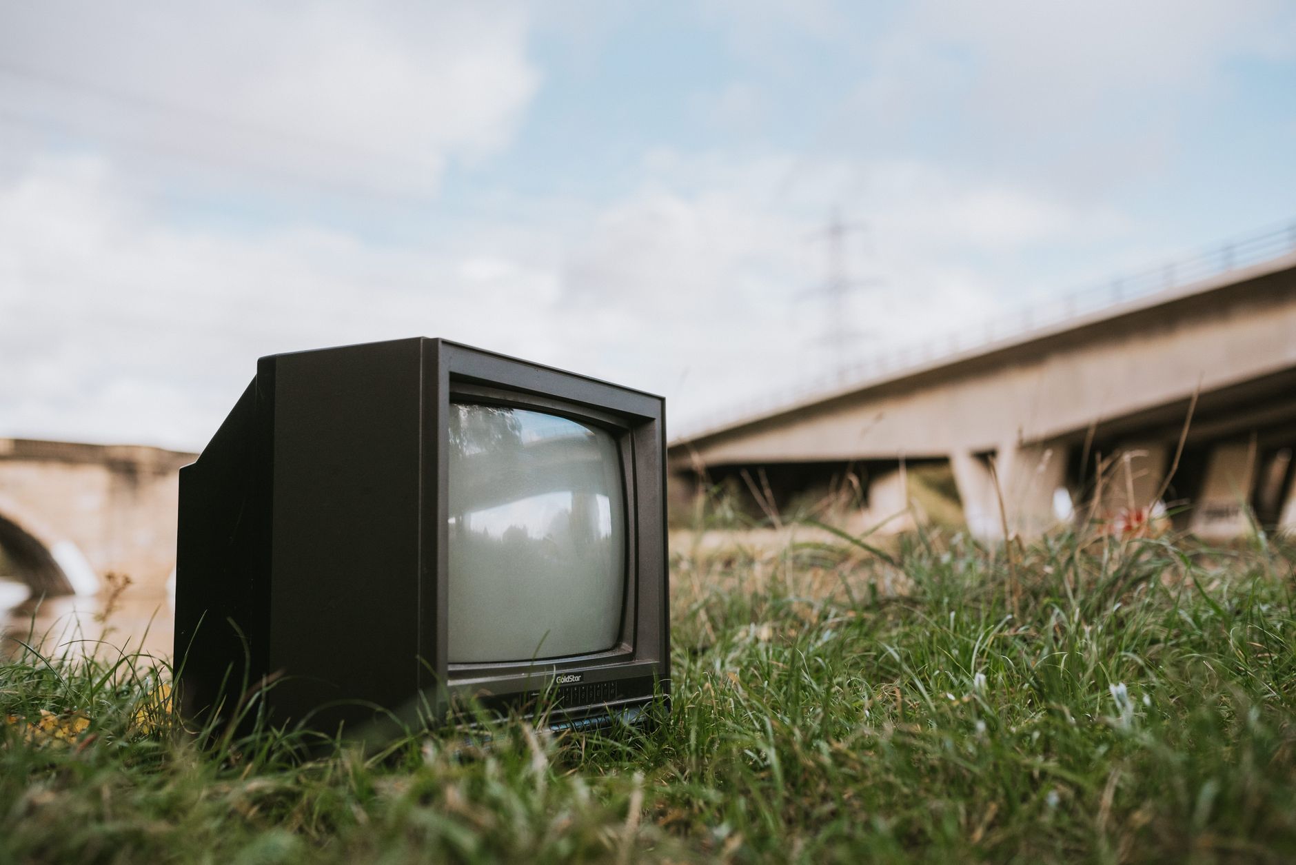Mały stary telewizor na trawie nad rzeką z mostem w tle