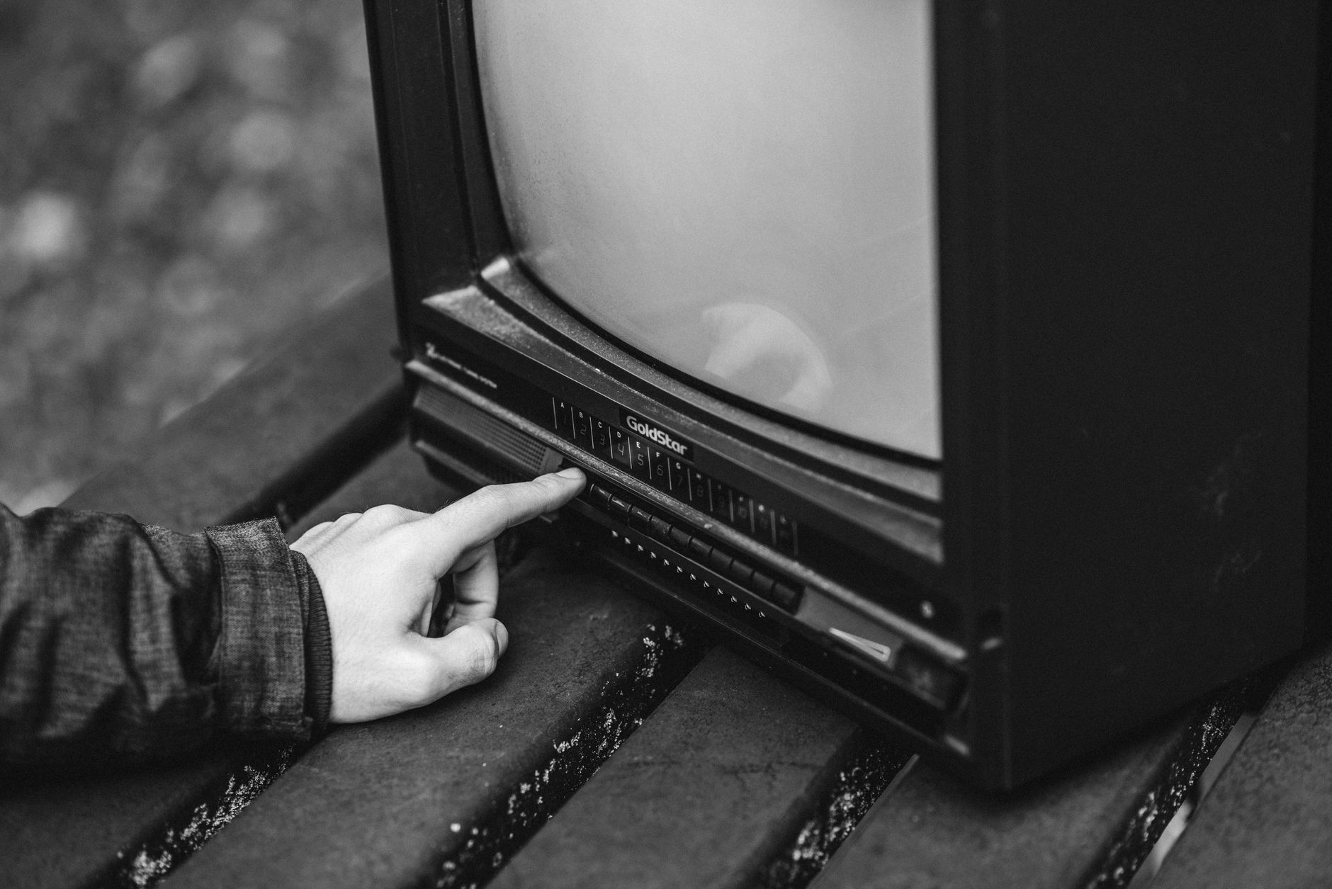 Mężczyzna naciska przyciski starego telewizora stojącego na drewnianym stoliku Mężczyzna naciska przyciski starego telewizora stojącego na drewnianym stoliku